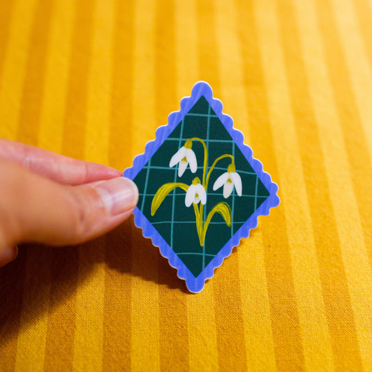 Diamond-shaped sticker with floral design held by a hand on a yellow textured background