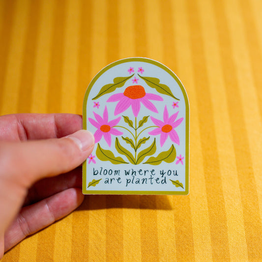 Hand holding a decorative sticker with floral design and text on a yellow background