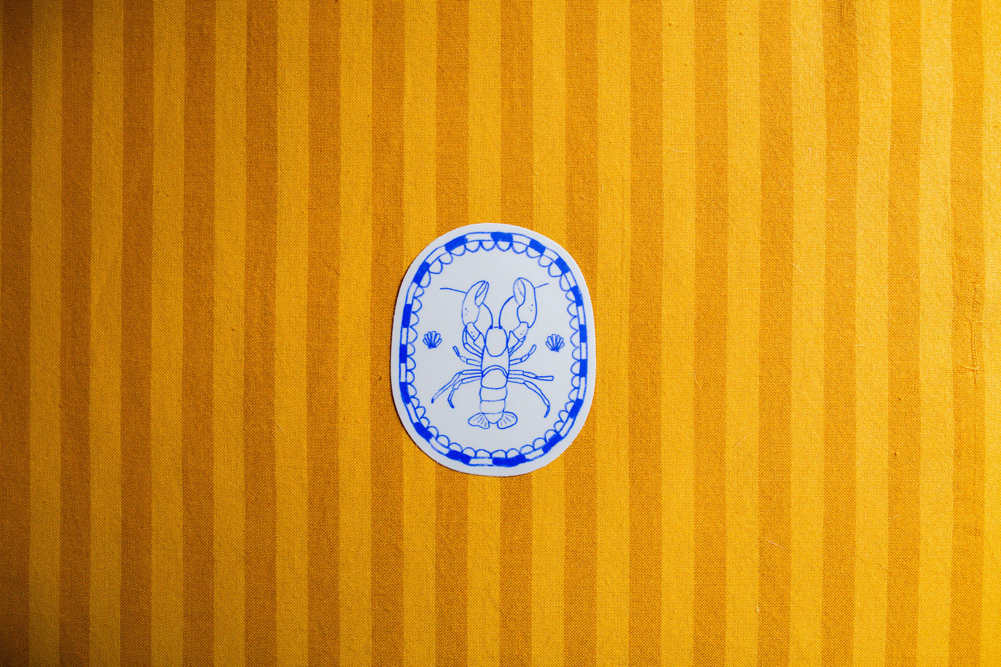 Decorative blue and white illustration of a lobster on a sticker on a yellow striped background
