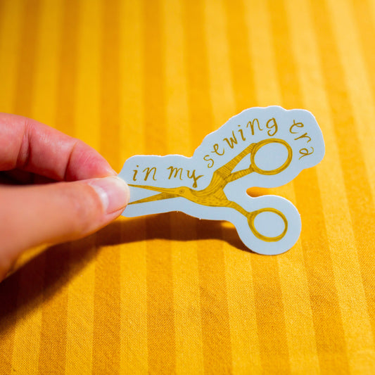 Hand holding a sticker with scissors and text on a yellow background