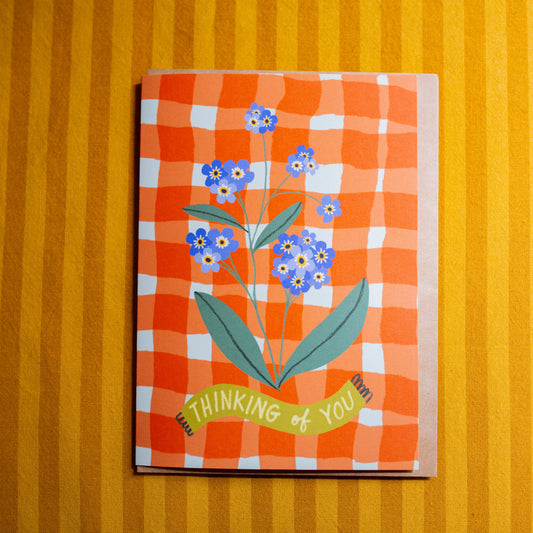 Card with floral design and 'Thinking of You' text on an orange checkered pattern against a striped yellow background