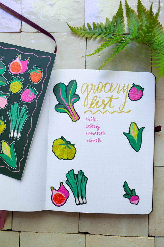 Notebook with colorful vegetable illustrations stickers and 'grocery list' text on a tile surface