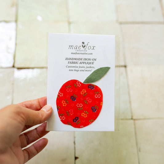 Handmade appliqué patch shaped like a apple, crafted from mixed vintage fabrics in rich red tones with a textured green leaf top, slightly imperfect, charming handmade finish, designed for decorating jackets, jeans, or tote bags.