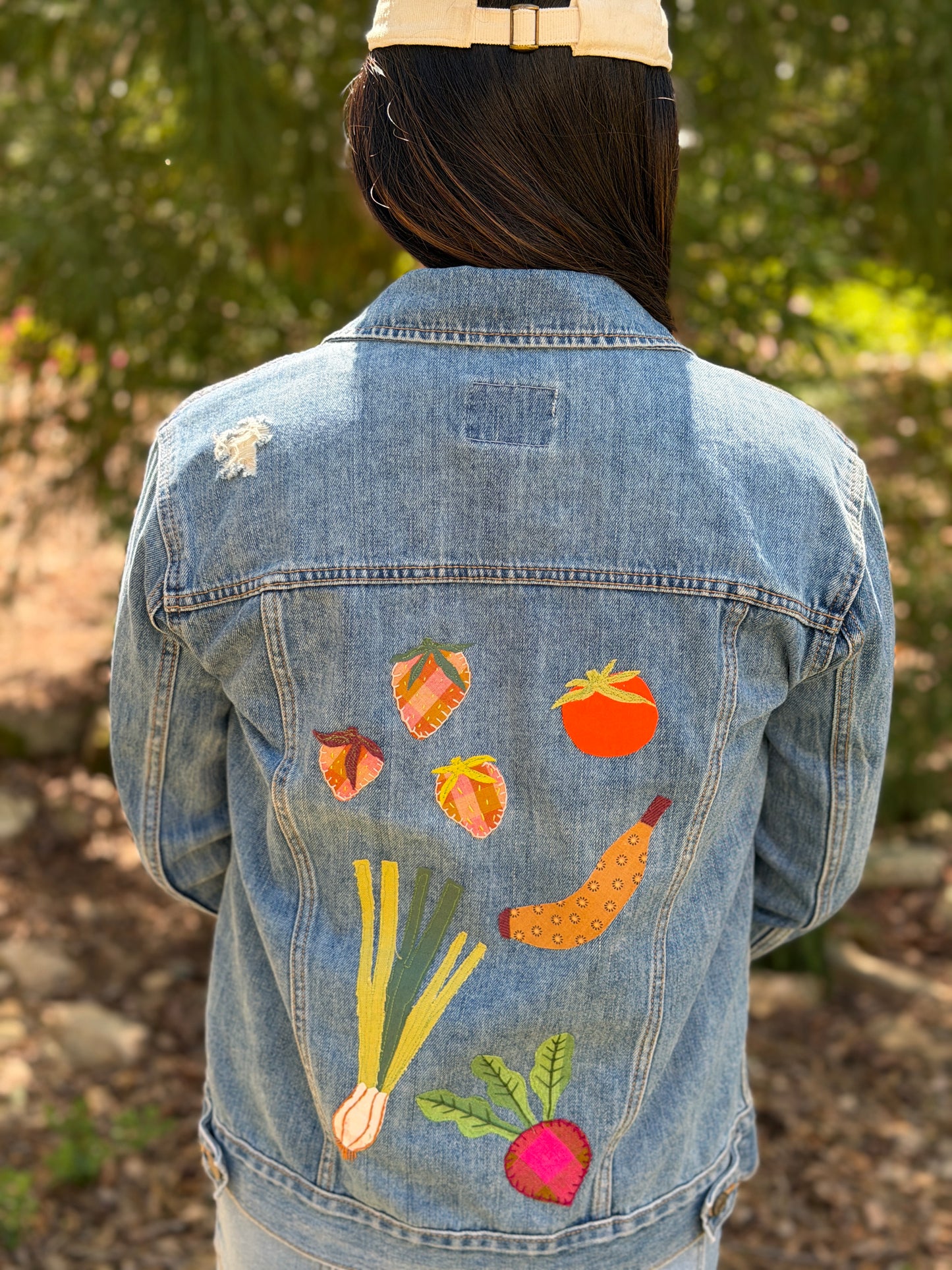 girl wearing a jeans jacket with a variety of applique patches on it shaped like strawberries, a tomato, green onions, a banana, and a beet