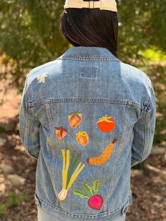 girl wearing a jeans jacket with a variety of applique patches on it shaped like strawberries, a tomato, green onions, a banana, and a beet