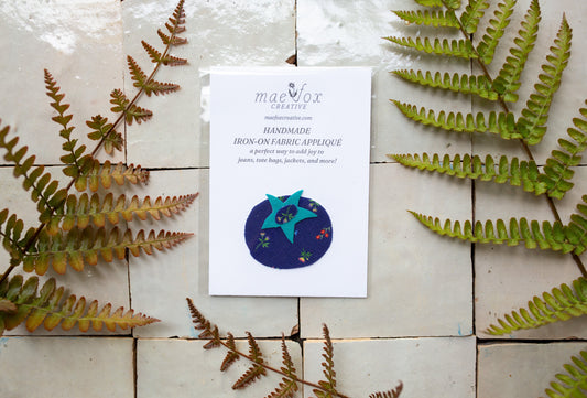 handmade applique fabric patch shaped like a blueberry, made with dark blue floral fabric and bright blue fabric accent