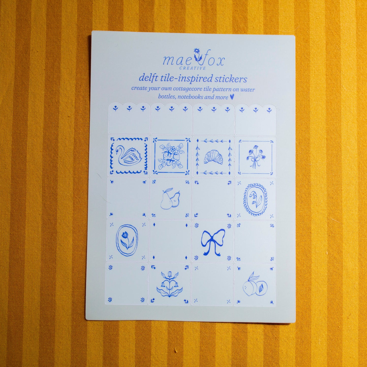 Sheet of blue delft tile-inspired stickers on a fabric surface