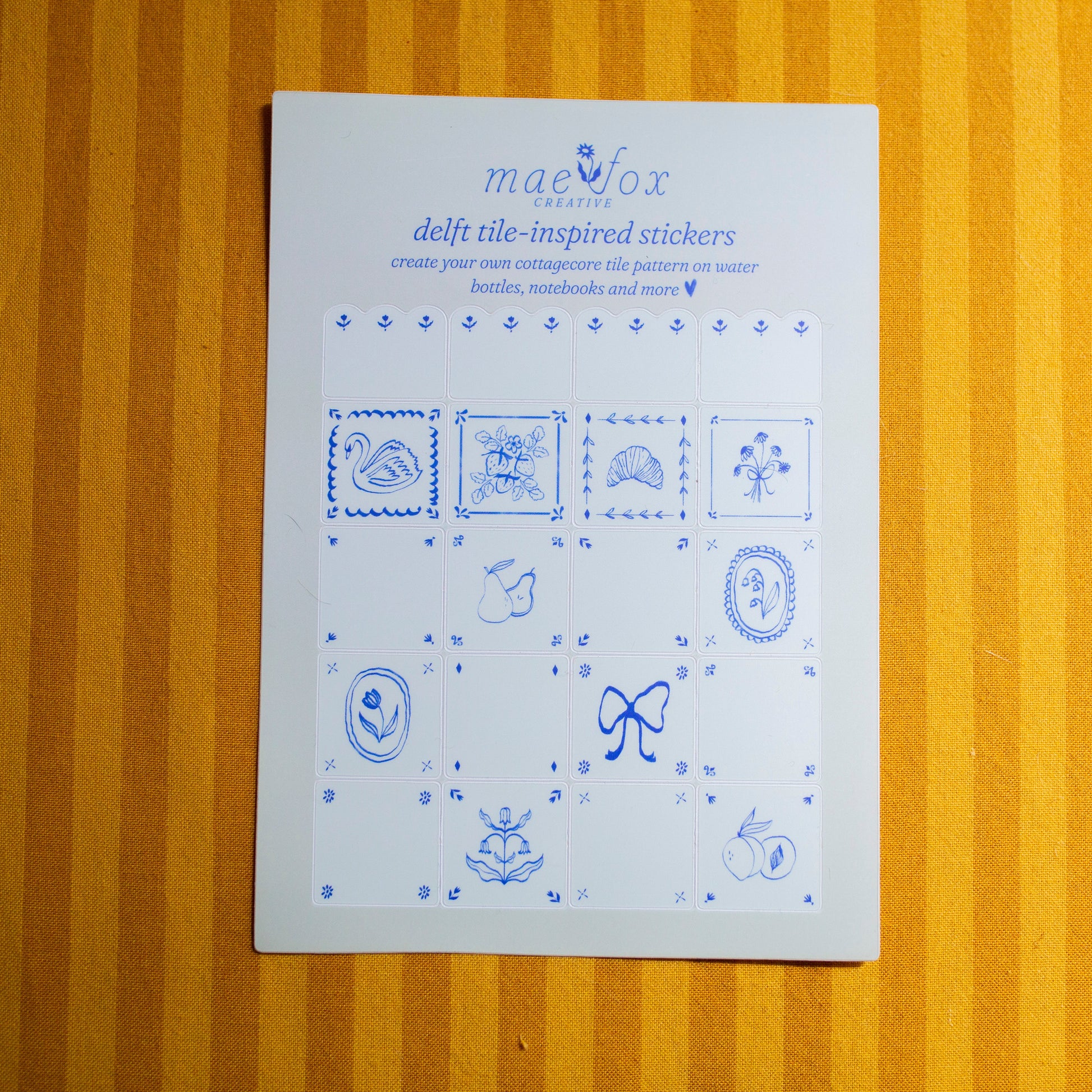 Sheet of blue delft tile-inspired stickers on a fabric surface