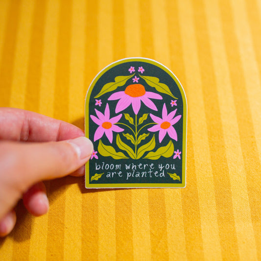 Hand holding a floral sticker with text on a yellow striped background