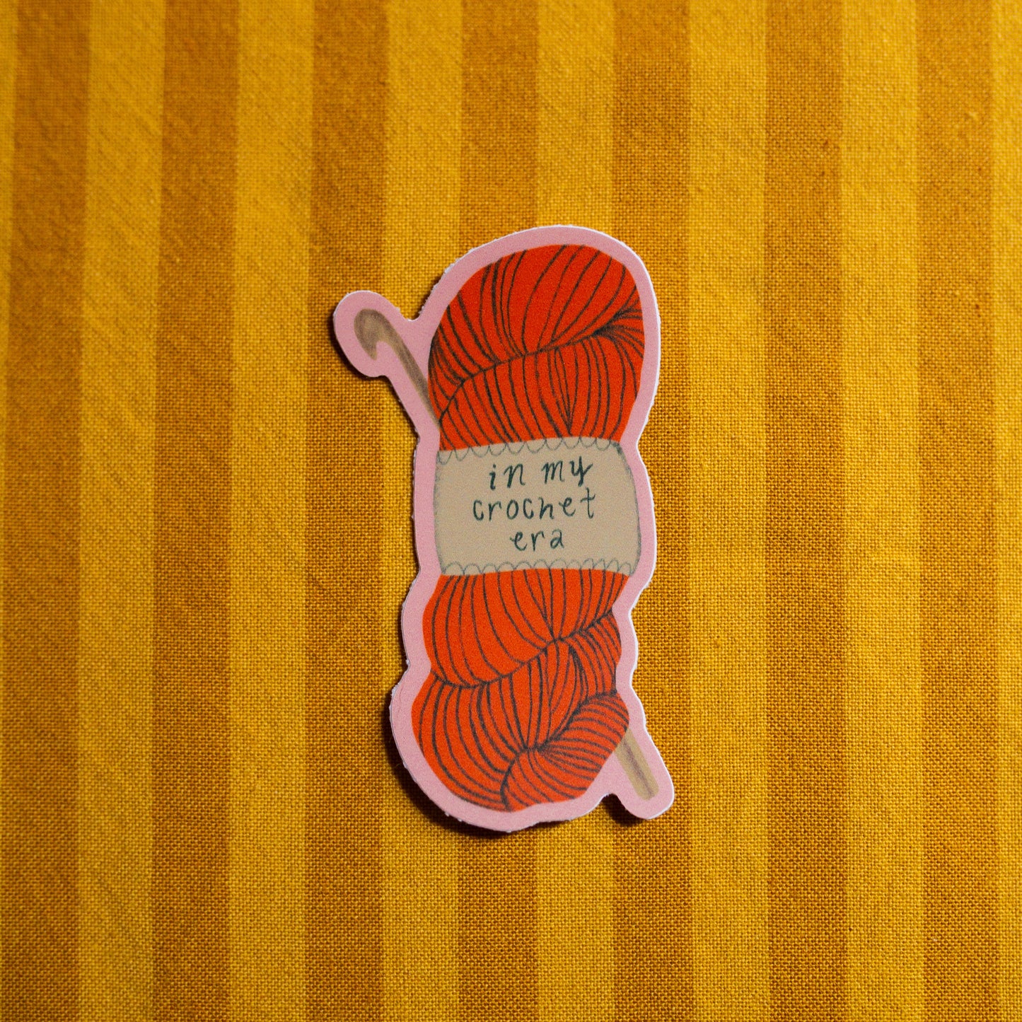 Sticker of a red yarn ball with a label on a yellow striped background