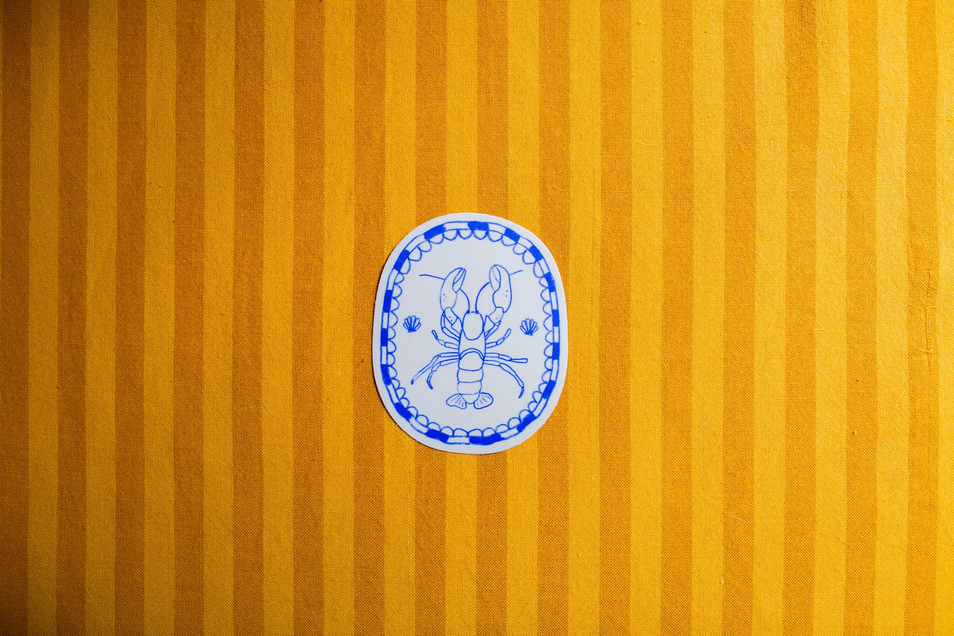 Decorative blue and white illustration of a lobster on a sticker  on a yellow striped background