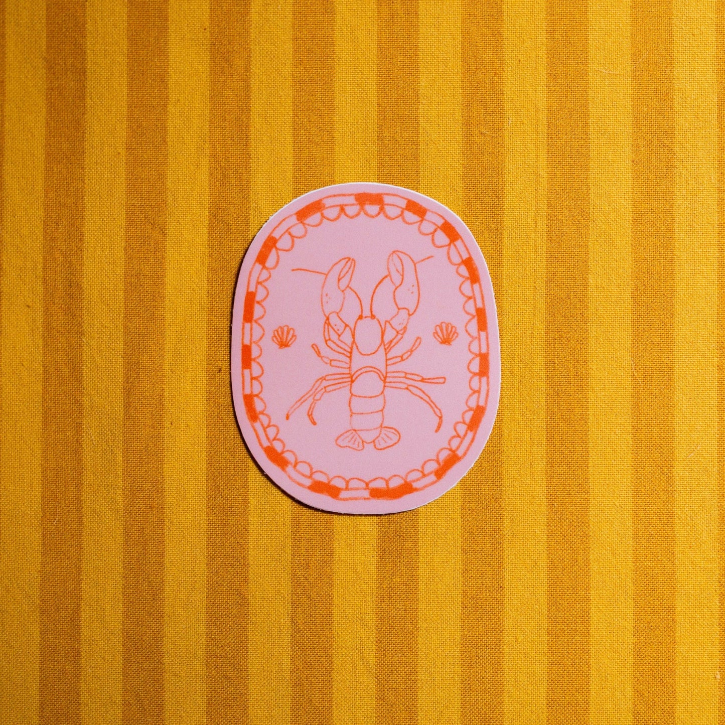 Pink circular sticker with a design of a lobster on a yellow striped background
