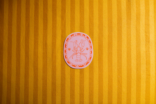 Pink circular sticker with a design of a lobster on a yellow striped background