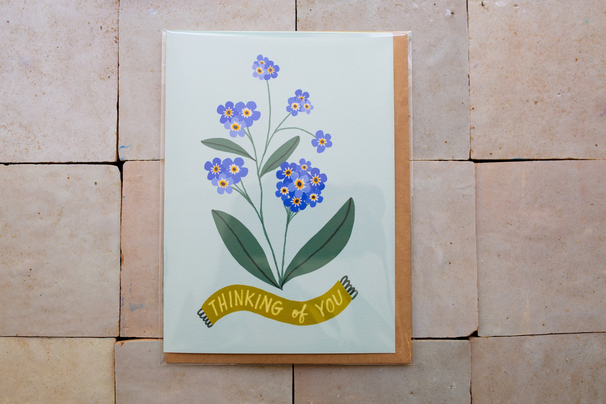 Card with floral design and 'Thinking of You' banner on a stone surface