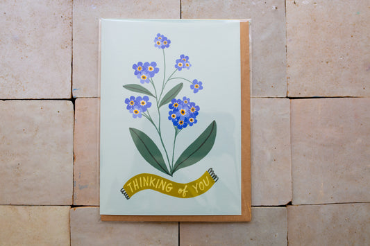 Card with floral design and 'Thinking of You' banner on a stone surface