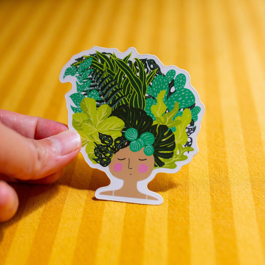 Sticker of a person with green leaves on their head held by a hand on a yellow background