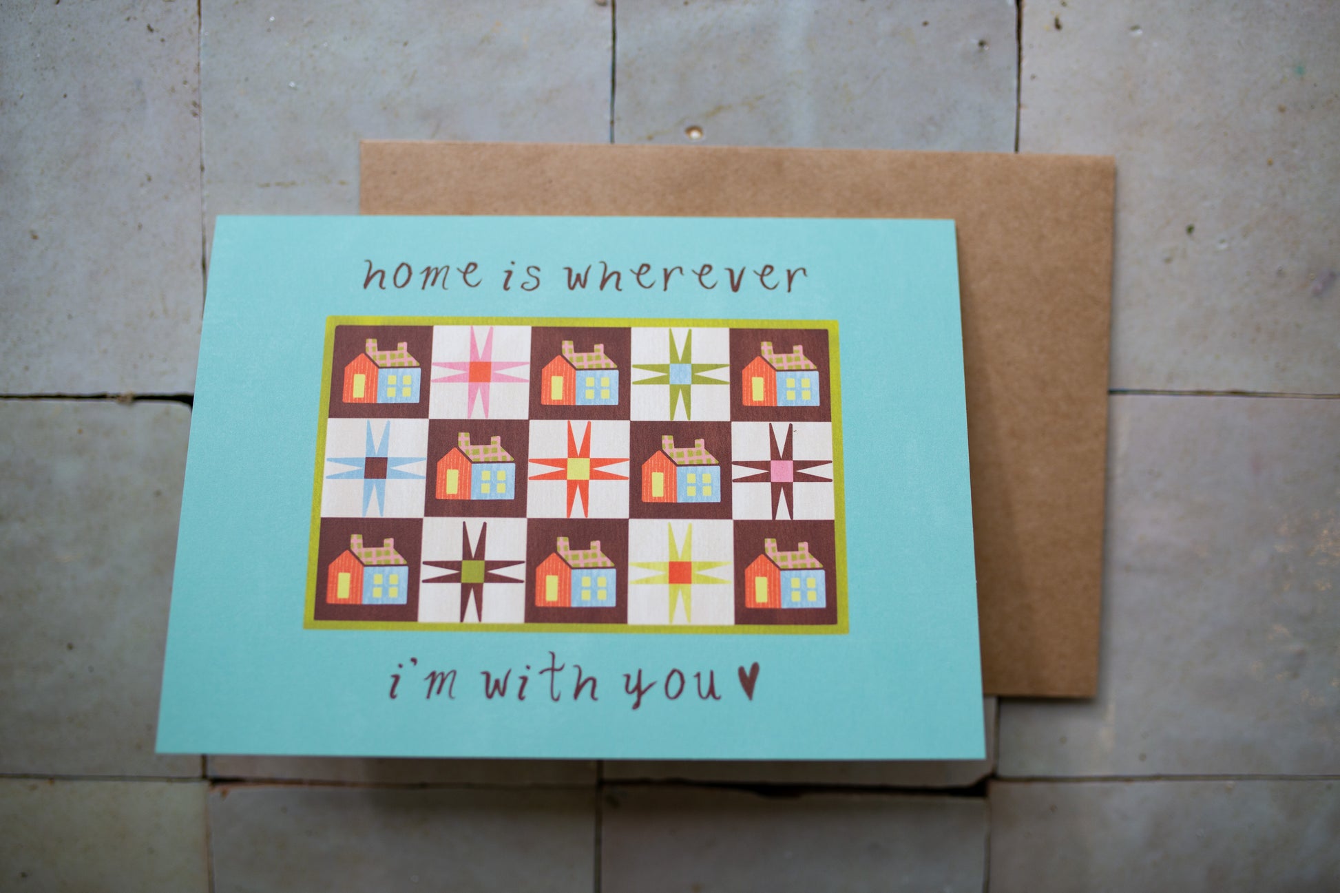 Card with quilt design and text 'home is wherever I'm with you' on a tile surface