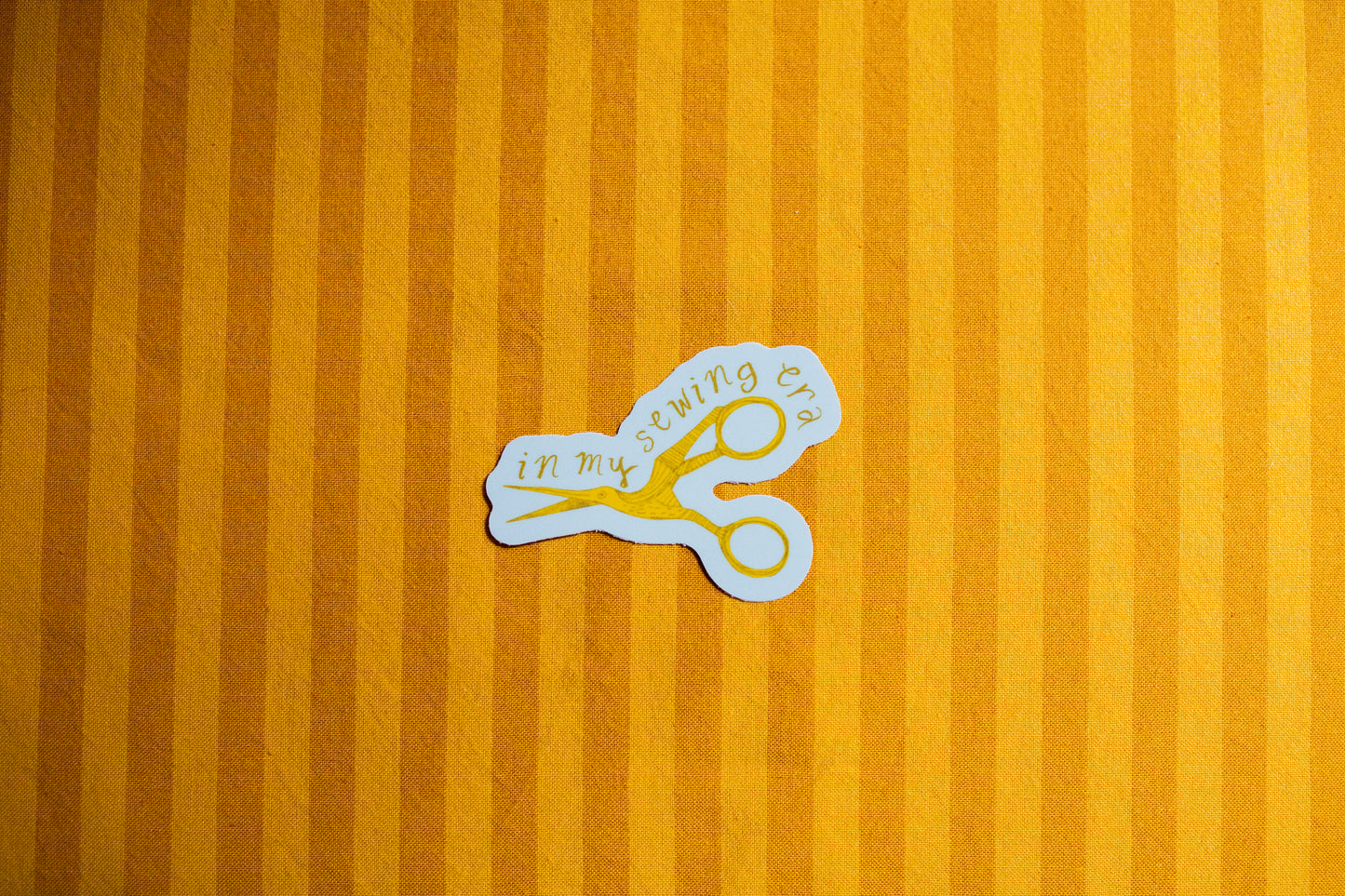 Sticker of scissors with text that says "In my sewing era" on a yellow striped background