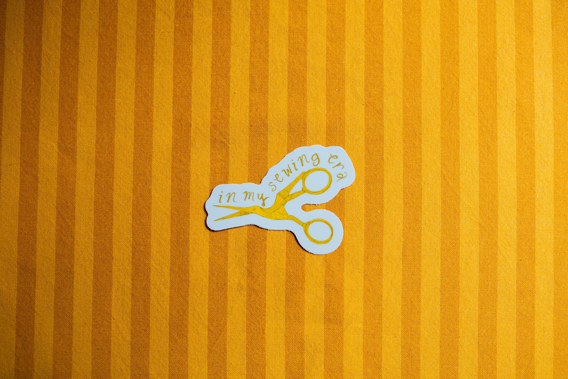 Sticker of scissors with text that says "In my sewing era" on a yellow striped background