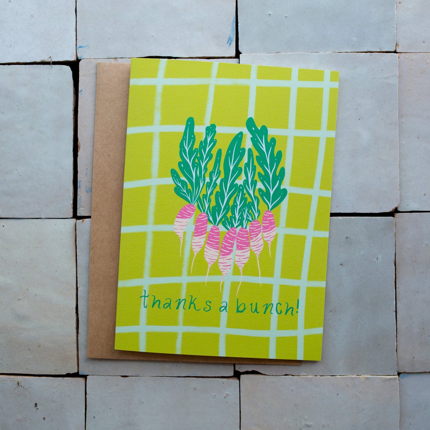 Green checkered card with a radish design and 'thanks a bunch!' text photographed on a tiled surface