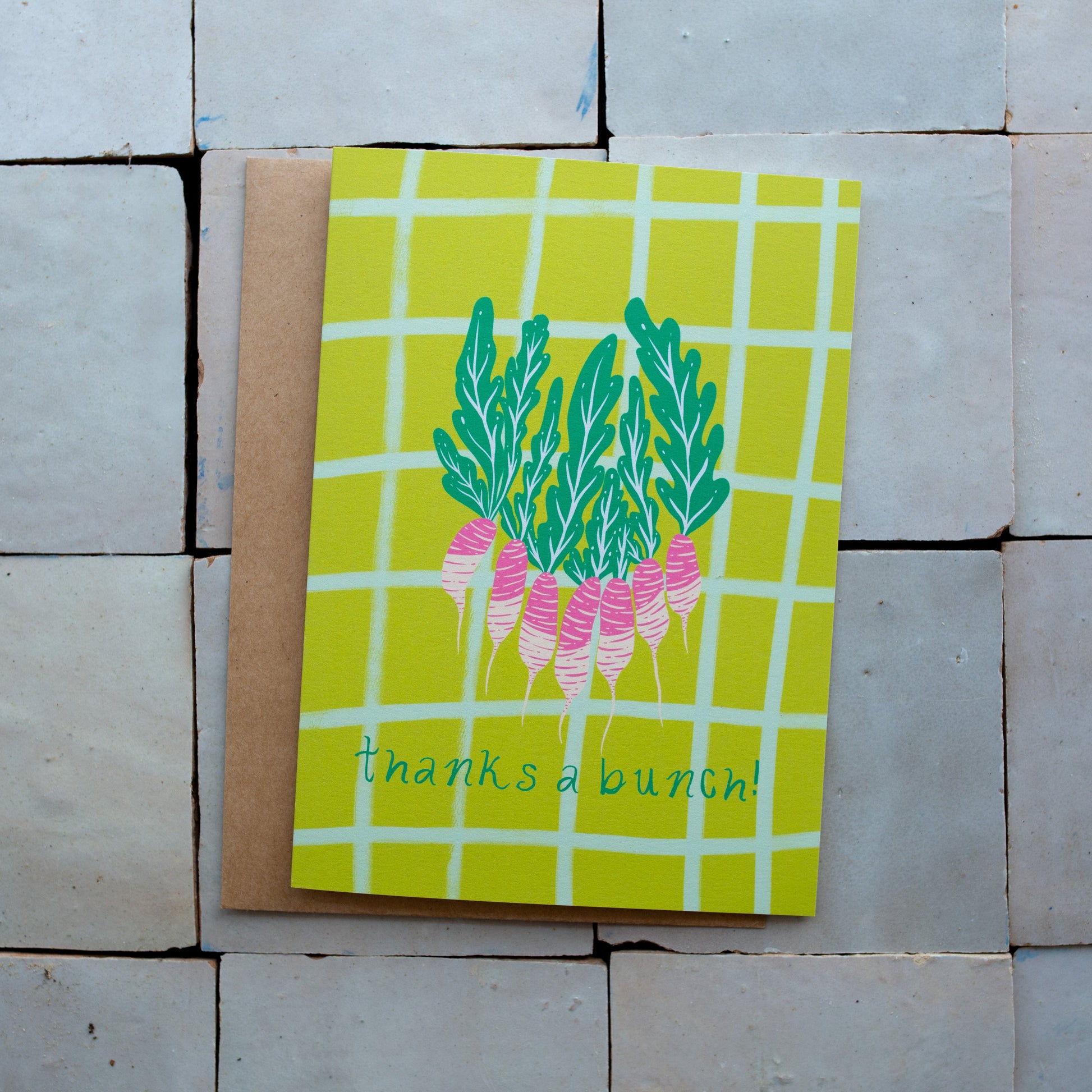 Green checkered card with a radish design and 'thanks a bunch!' text photographed on a tiled surface