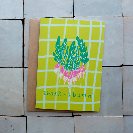 Green checkered card with a radish design and 'thanks a bunch!' text photographed on a tiled surface