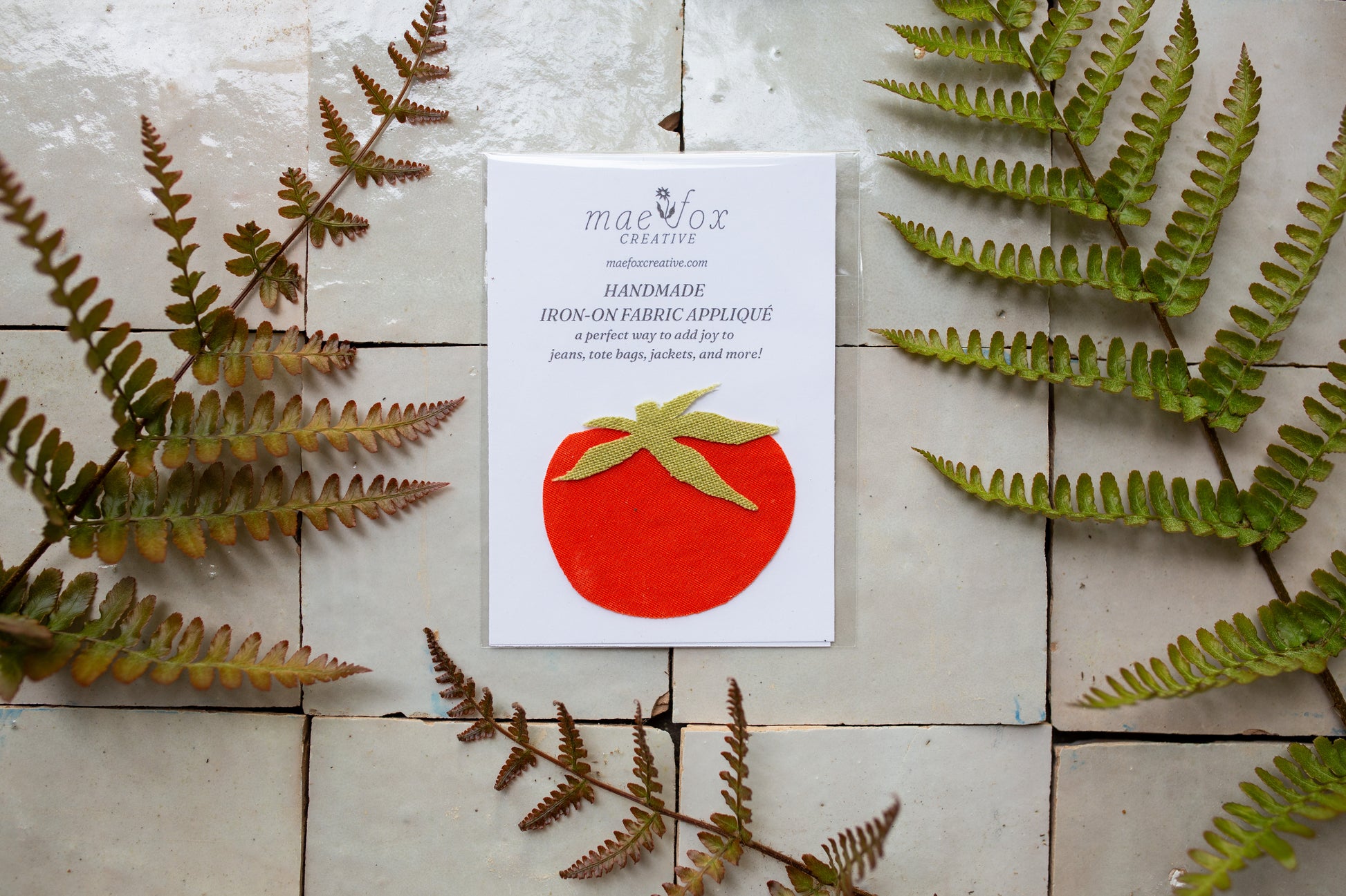 Handmade appliqué patch shaped like a tomato, crafted from mixed vintage fabrics in rich red tones with a textured green leaf top, featuring visible stitching and a slightly imperfect, charming handmade finish, designed for decorating jackets, jeans, or tote bags.