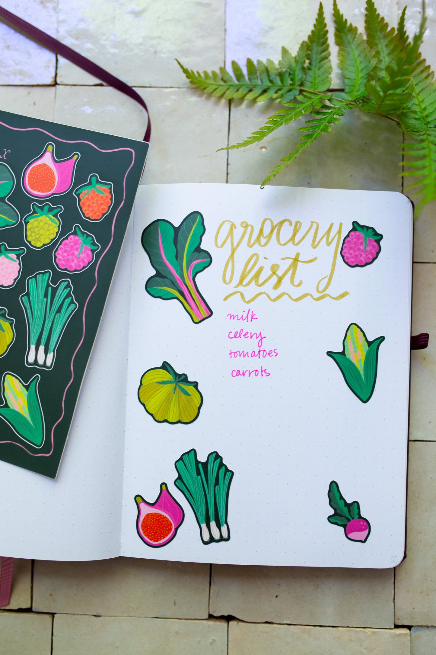 Notebook with colorful vegetable illustrations stickers and 'grocery list' text on a tile surface