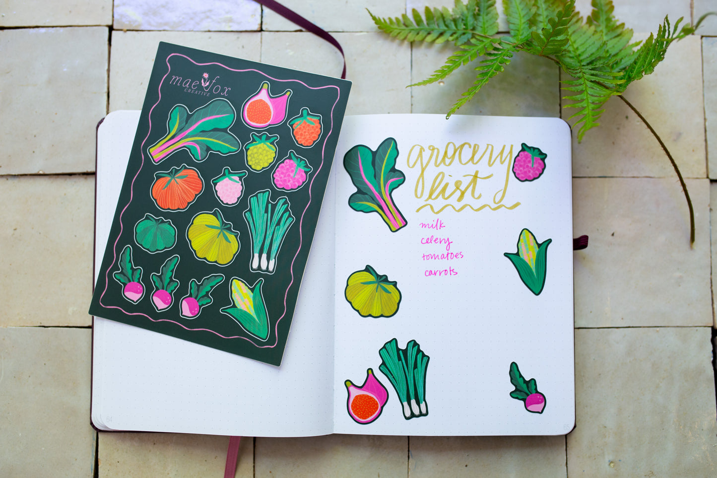 Open notebook with vegetable illustrations stickers and a notebook on a tilesurface.