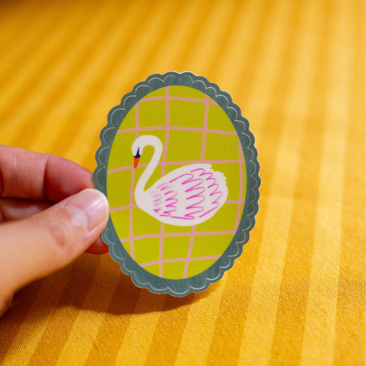 Hand holding a sticker of a swan on a yellow textured background