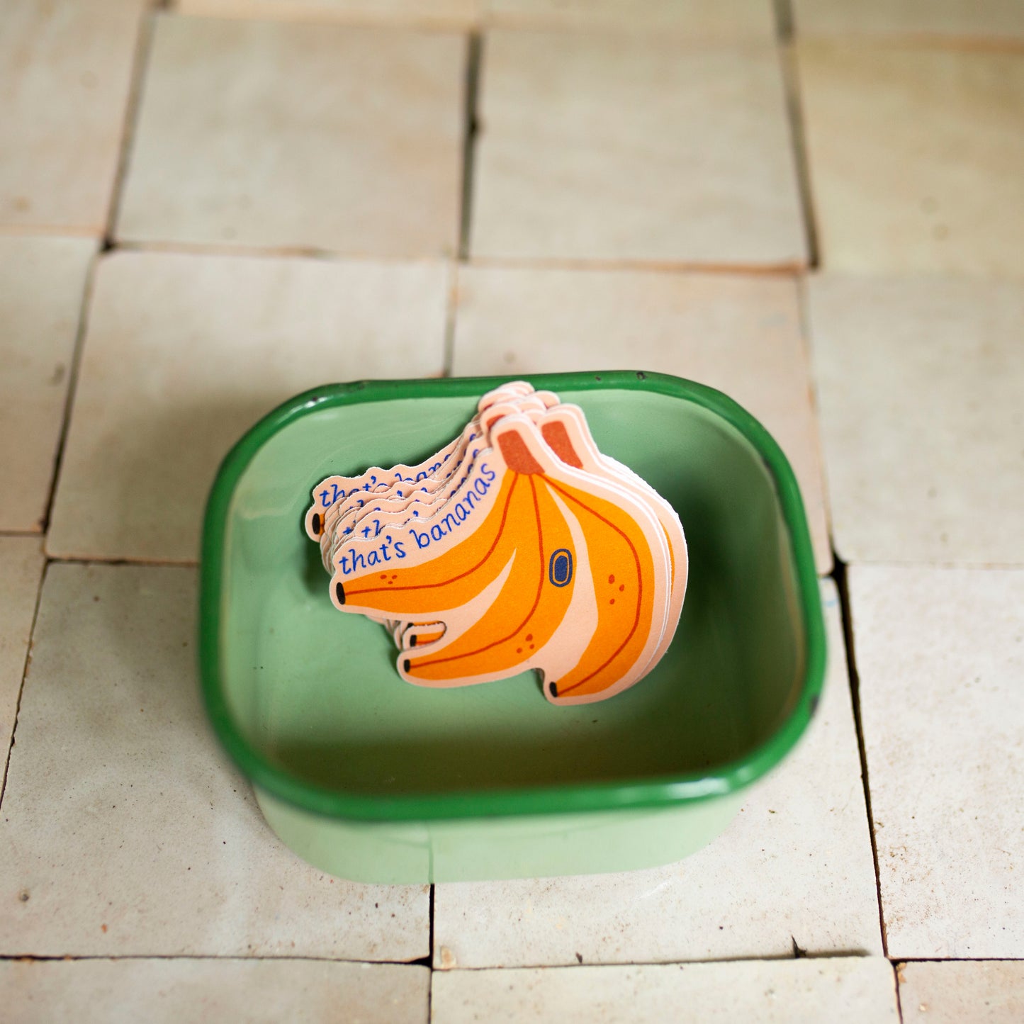 a stack of banana stickers in a green enamel container