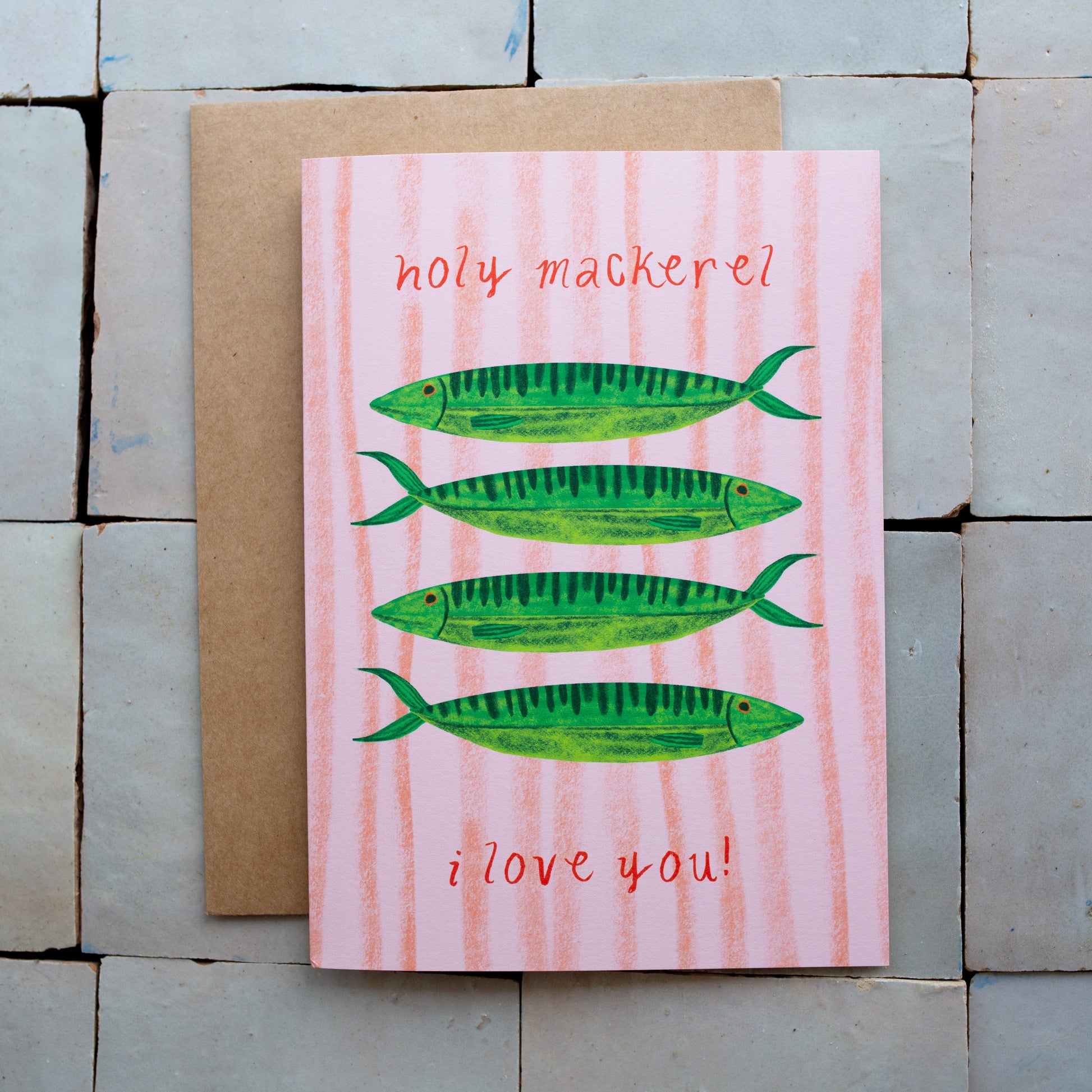 Card with green fish illustrations and text on a pink background, placed on a stone surface.