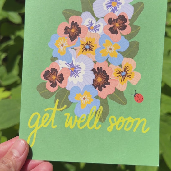 Video of a card that says get well soon with a pansies and a lady bug on a green background