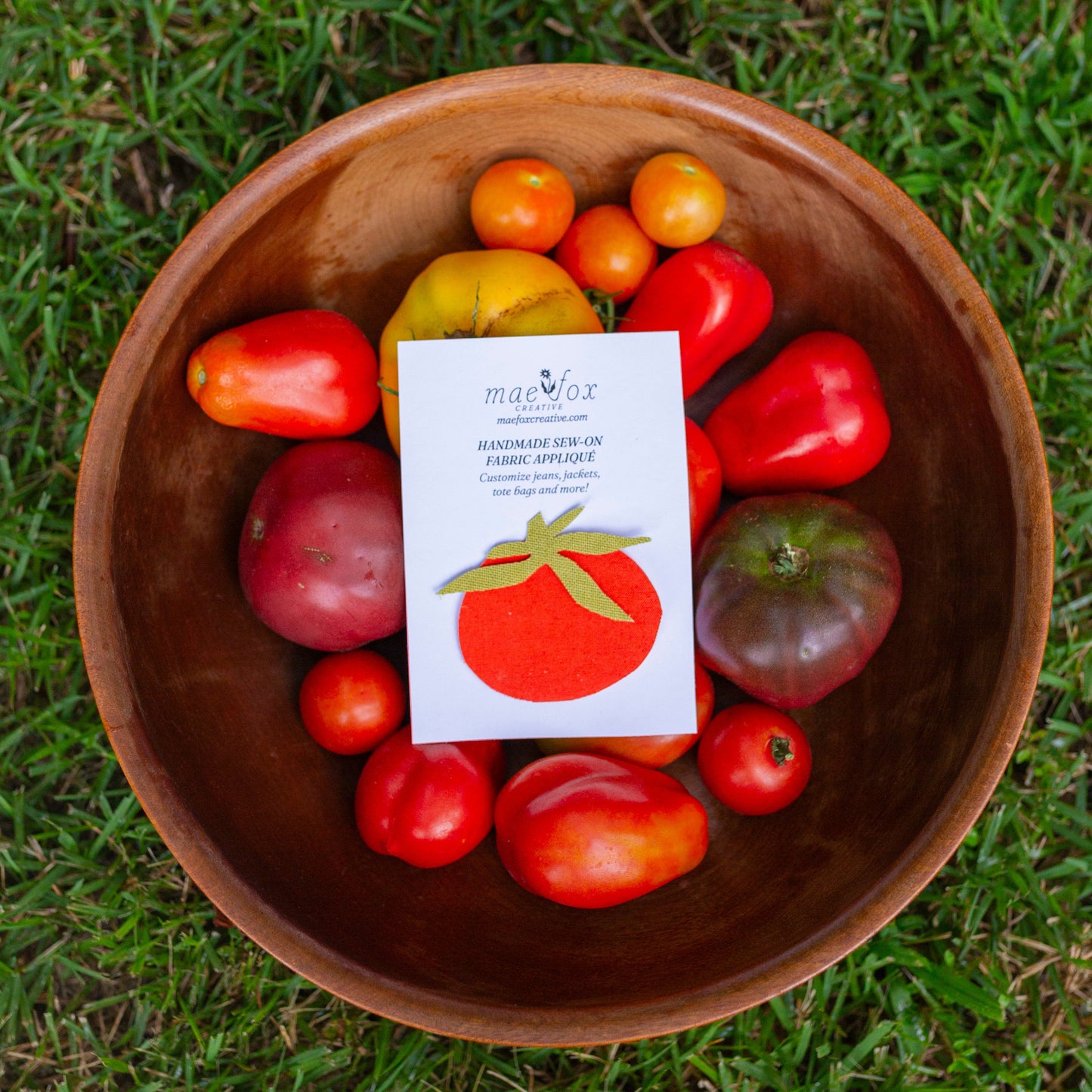 A wooden bowl filled with assorted fresh tomatoes and a stomato fabric patch